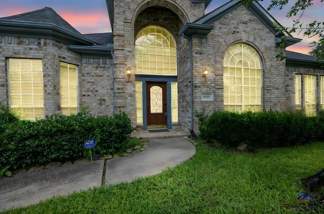 Home features a charming brick exterior with large arched windows and a welcoming front entrance. The well-maintained landscaping includes lush greenery, creating an inviting curb appeal. | Image 5