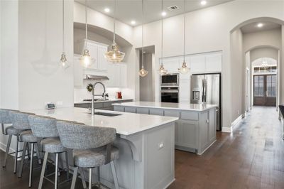 Kitchen with an island with sink, decorative light fixtures, white cabinetry, stainless steel appliances, and dark hardwood / wood-style floors | Image 2