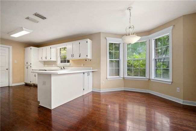 Kitchen featuring light countertops, dark wood finished floors, a peninsula, white cabinets, and pendant lighting | Image 11
