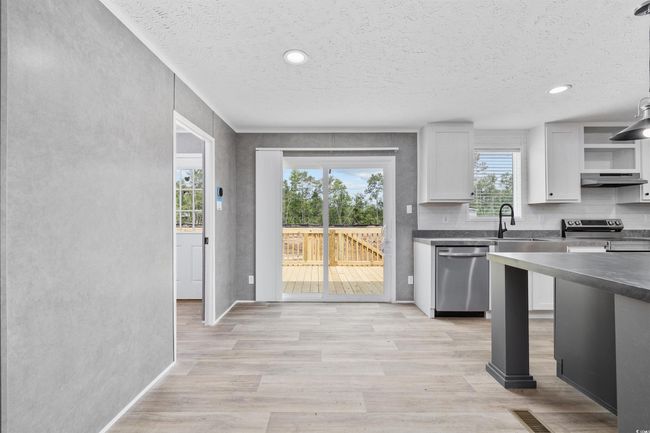 Kitchen featuring appliances with stainless steel finishes, under cabinet range hood, open shelves, dark countertops, and light wood-type flooring | Image 16