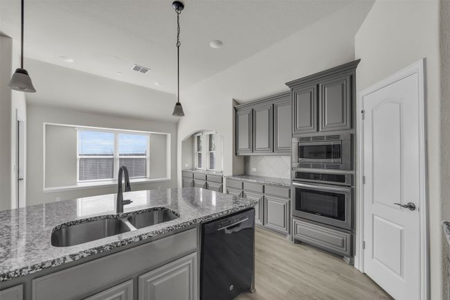 Kitchen featuring appliances with stainless steel finishes, light wood-type flooring, light stone counters, sink, and decorative light fixtures | Image 20