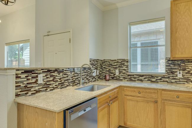 Kitchen featuring dishwasher, backsplash, ornamental molding, light stone countertops, and light brown cabinets | Image 14