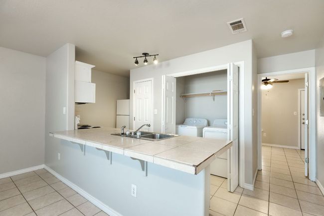 Kitchen with a peninsula, a kitchen breakfast bar, washing machine and dryer, white cabinetry, and light tile patterned flooring | Image 7