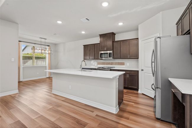 Kitchen with appliances with stainless steel finishes, a sink, light wood-style floors, light countertops, and dark brown cabinetry | Image 10