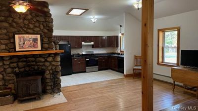 Kitchen with a fireplace, vaulted ceiling, light hardwood / wood-style flooring, black appliances, and dark brown cabinetry | Image 3