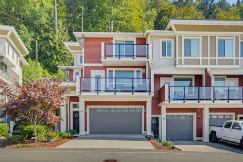 Multilevel townhouse exterior with red siding and light trim, featuring balconies with glass railings, an integrated garage, and a paved driveway | Card Image