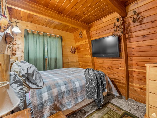 Carpeted bedroom featuring wooden walls and a wooden ceiling with exposed beams | Image 12