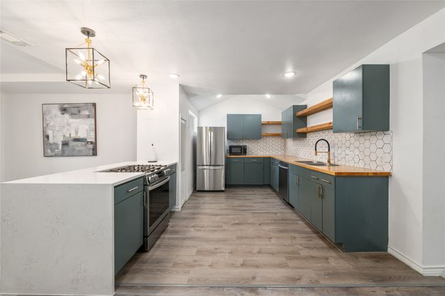 Kitchen with stainless steel appliances, a sink, open shelves, lofted ceiling, and butcher block counters | Image 7