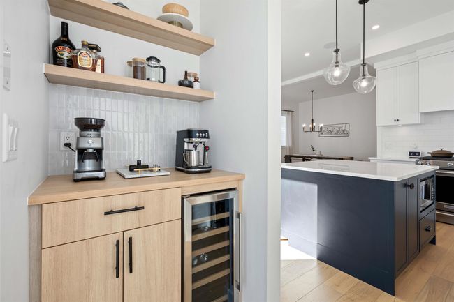 Kitchen with light wood finished floors, open shelves, stove, wine cooler, and light countertops | Image 13