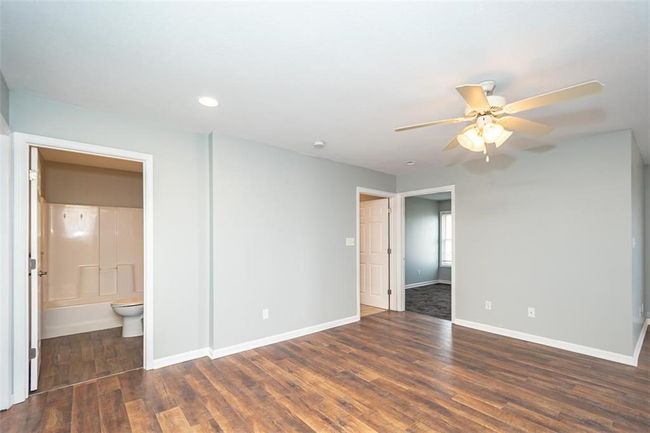 Unfurnished bedroom with ceiling fan, connected bathroom, baseboards, and wood finished floors | Image 6