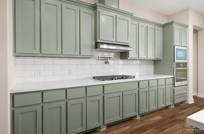 Kitchen featuring green cabinets, light countertops, under cabinet range hood, dark wood finished floors, and stainless steel appliances | Image 6