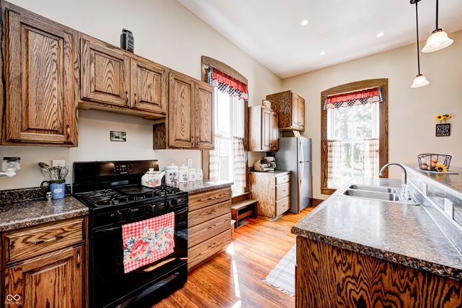 kitchen featuring black range with gas stovetop, light wood-style flooring, freestanding refrigerator, dark countertops, and a sink | Image 22