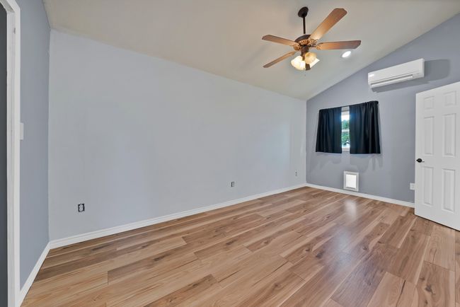 Empty room with a wall unit AC, light wood-type flooring, a ceiling fan, and high vaulted ceiling | Image 9