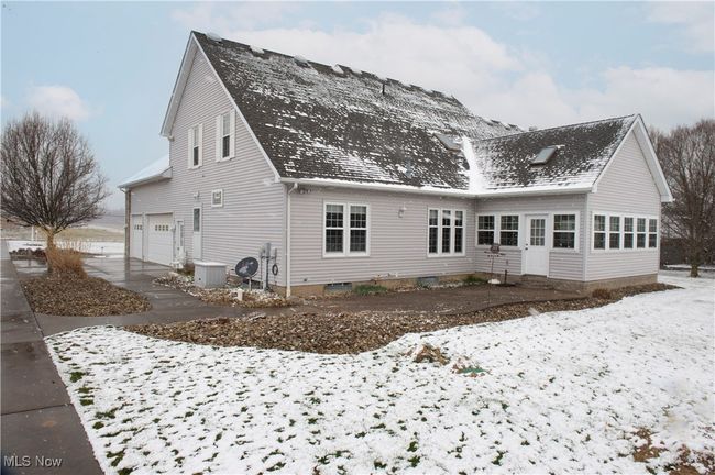 Snow covered back of property with concrete driveway, cooling unit, an attached garage, and roof with shingles | Image 23