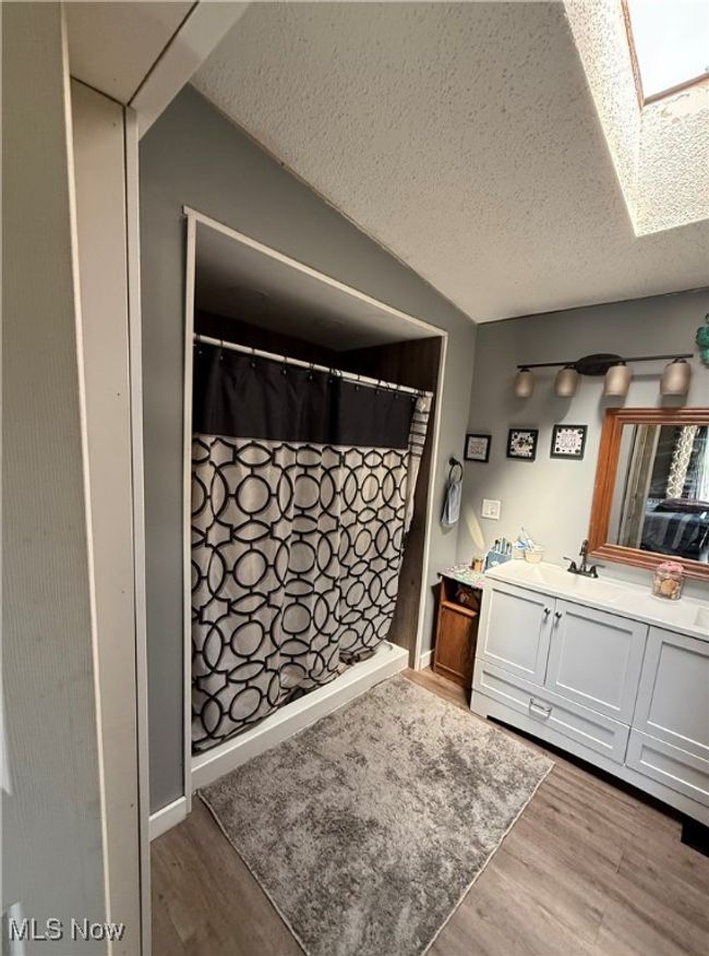 Full bathroom featuring a skylight, wood finished floors, vanity, and a textured ceiling | Image 24
