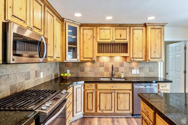 Kitchen with stainless steel appliances, dark stone countertops, glass insert cabinets, light wood-style floors, and recessed lighting | Image 19