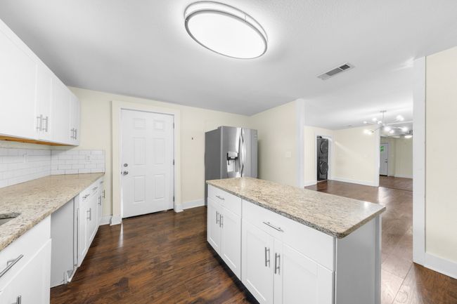 Kitchen featuring stainless steel fridge, decorative backsplash, dark wood-type flooring, a center island, and light stone countertops | Image 10