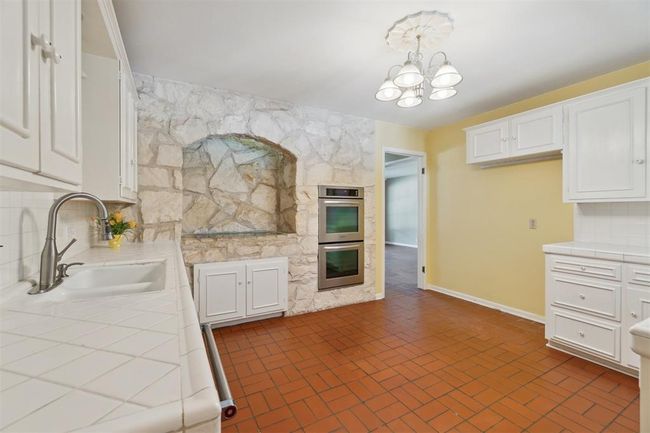 Kitchen with tile counters, stainless steel double oven, white cabinetry, a chandelier, and decorative backsplash | Image 14