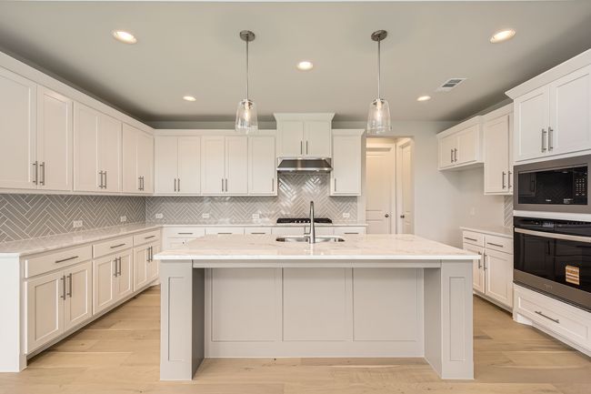 Kitchen featuring stainless steel appliances, under cabinet range hood, backsplash, light stone counters, and white cabinets | Image 11