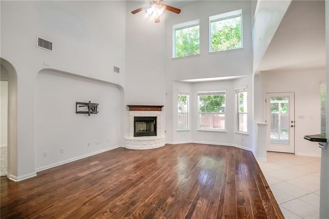 Unfurnished living room with a towering ceiling, ceiling fan, hardwood / wood-style floors, plenty of natural light, and a fireplace | Image 8