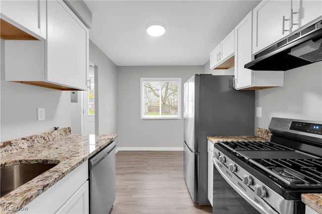 Kitchen featuring white cabinets, light wood-style flooring, stainless steel appliances, under cabinet range hood, and light stone countertops | Image 12
