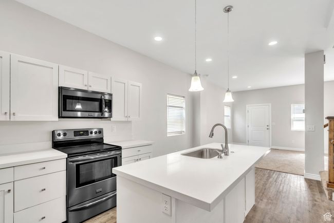 Kitchen with appliances with stainless steel finishes, white cabinets, light countertops, a center island with sink, and light wood finished floors | Image 13