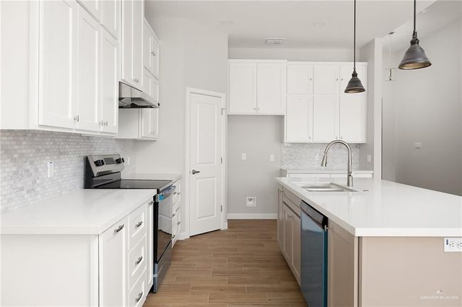 Kitchen featuring under cabinet range hood, white cabinetry, a sink, and appliances with stainless steel finishes | Image 7