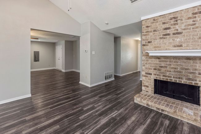 Unfurnished living room with baseboards, vaulted ceiling, dark wood-style flooring, a brick fireplace, and electric panel | Image 7