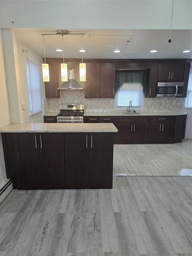Kitchen featuring light wood finished floors, decorative backsplash, stove, a sink, and exhaust hood | Image 9