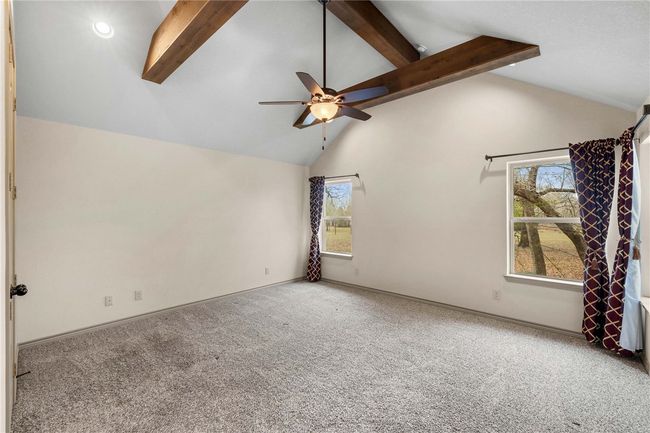 Carpeted empty room featuring high vaulted ceiling, beamed ceiling, baseboards, and ceiling fan | Image 11