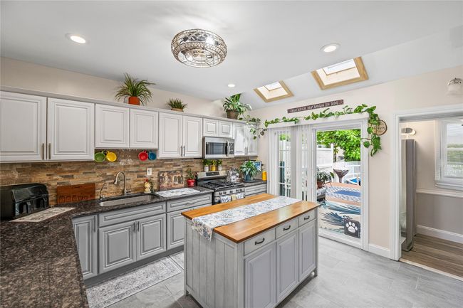 Kitchen with a sink, stainless steel appliances, a skylight, butcher block countertops, and gray cabinets | Image 14