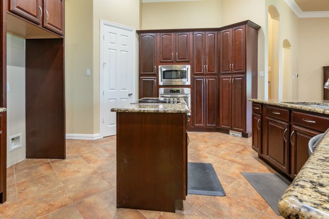 Kitchen featuring stainless steel appliances, ornamental molding, light stone countertops, arched walkways, and a center island | Image 9