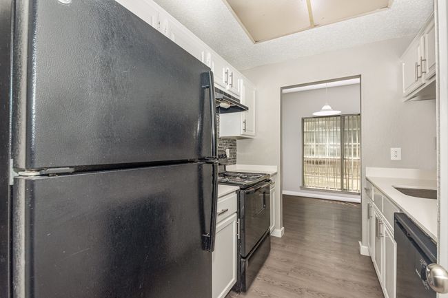 Kitchen featuring black appliances, wood finished floors, white cabinets, light countertops, and under cabinet range hood | Image 14