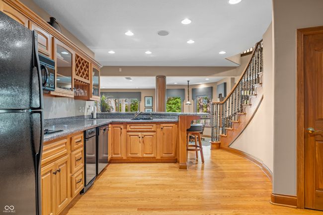 Bar kitchen with a sink, glass insert cabinets, black appliances, light wood-style flooring, and a peninsula | Image 63