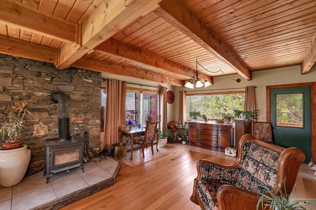 Sitting room featuring a wooden ceiling with exposed beams, a wood stove, light wood-type flooring, and a chandelier | Image 12