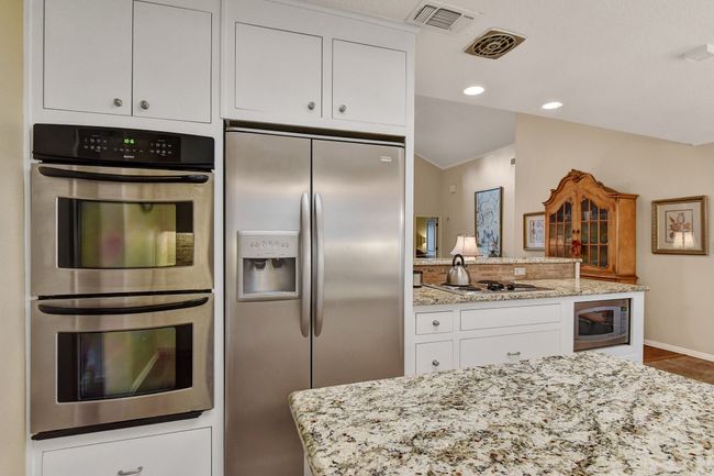 Kitchen featuring stainless steel appliances, white cabinetry, light stone countertops, a peninsula, and tile patterned floors | Image 17