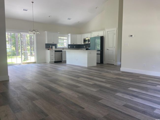 Kitchen with appliances with stainless steel finishes, open floor plan, white cabinetry, a center island, and dark wood-type flooring | Image 9