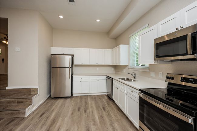 Kitchen with appliances with stainless steel finishes, white cabinetry, light countertops, light wood finished floors, and recessed lighting | Image 8