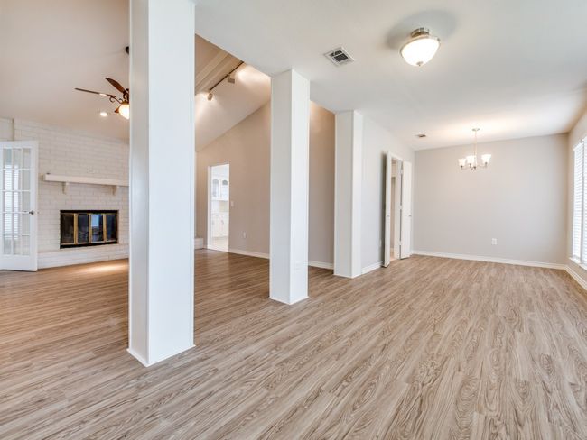 Unfurnished living room with a chandelier, a ceiling fan, light wood-style flooring, a fireplace, and baseboards | Image 4