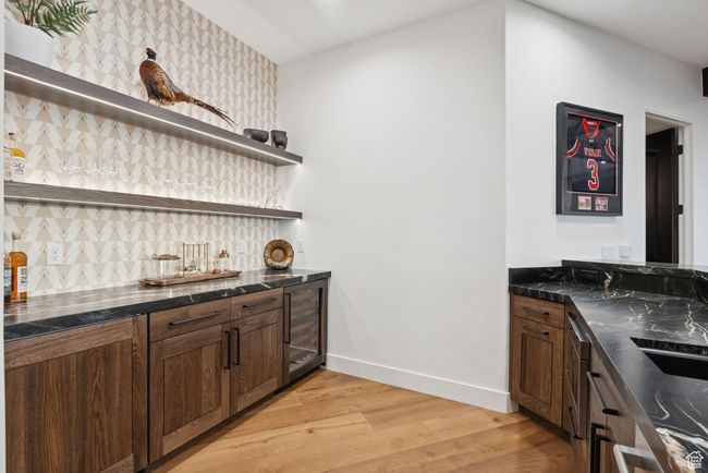 Indoor wet bar featuring light wood-type flooring, decorative backsplash, and wine cooler | Image 52