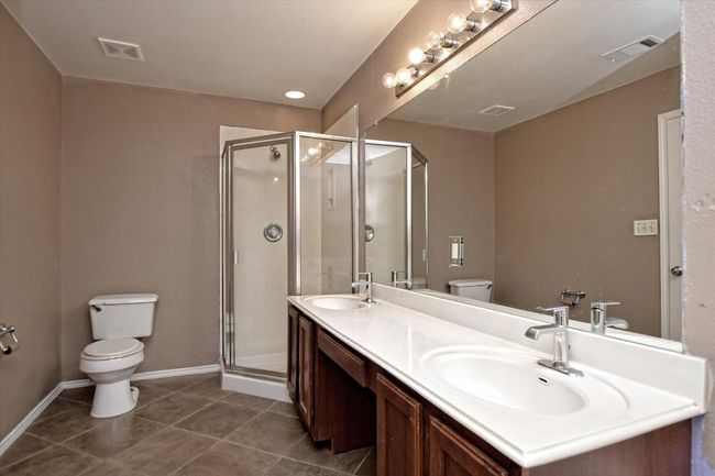 Bathroom with toilet, double vanity, a shower stall, and tile patterned flooring | Image 18