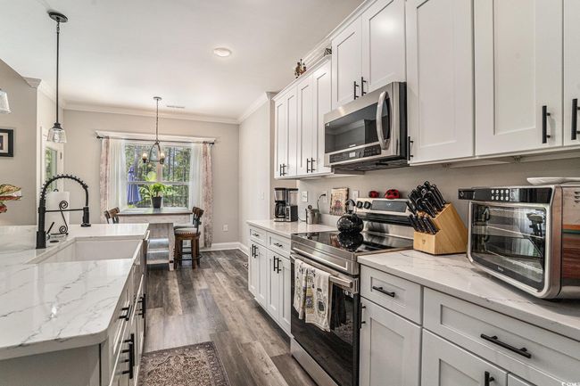 Kitchen featuring stainless steel appliances, a sink, ornamental molding, a chandelier, and white cabinets | Image 11