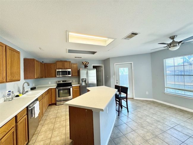 Kitchen featuring appliances with stainless steel finishes, a kitchen island, brown cabinets, light countertops, and light tile patterned floors | Image 6