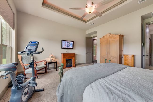 Bedroom featuring carpet flooring, multiple windows, a raised ceiling, and a glass covered fireplace | Image 27