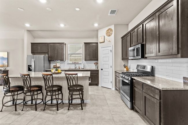 Kitchen with stainless steel appliances, a center island, dark brown cabinets, backsplash, and recessed lighting | Image 4