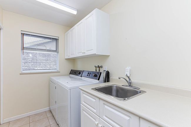 Laundry area featuring cabinet space, baseboards, separate washer and dryer, a sink, and light tile patterned flooring | Image 21