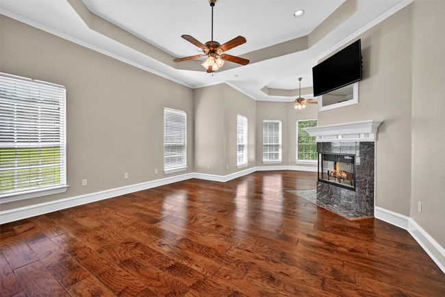 Unfurnished living room with a ceiling fan, a raised ceiling, a fireplace, baseboards, and hardwood / wood-style floors | Image 21