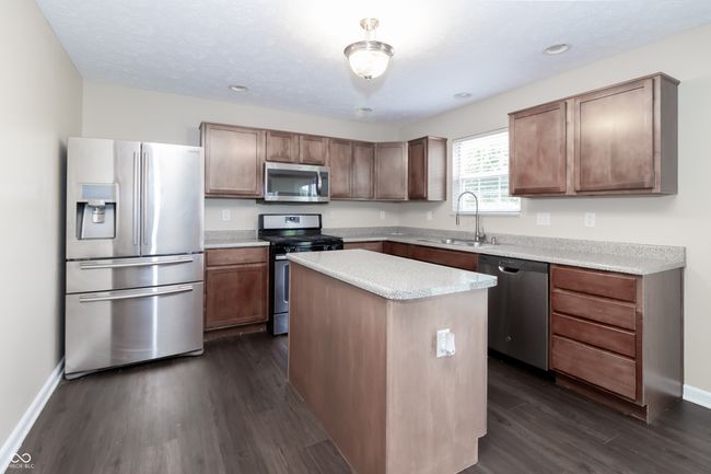 kitchen featuring appliances with stainless steel finishes, dark wood-type flooring, a kitchen island, light countertops, and recessed lighting | Image 9