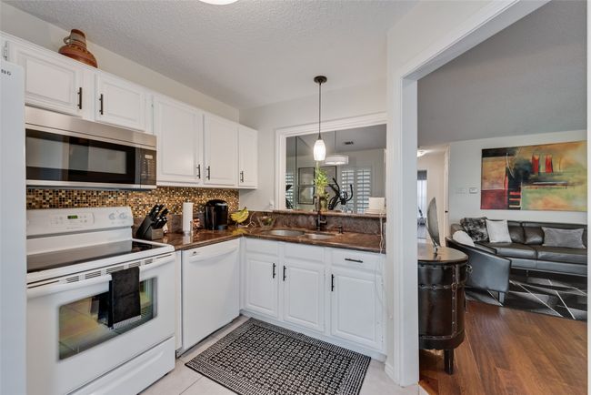 Kitchen featuring white appliances, white cabinetry, decorative light fixtures, tasteful backsplash, and a textured ceiling | Image 7