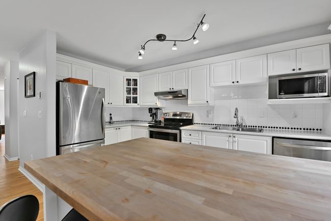 Kitchen with white cabinetry, wooden counters, under cabinet range hood, appliances with stainless steel finishes, and a sink | Image 14
